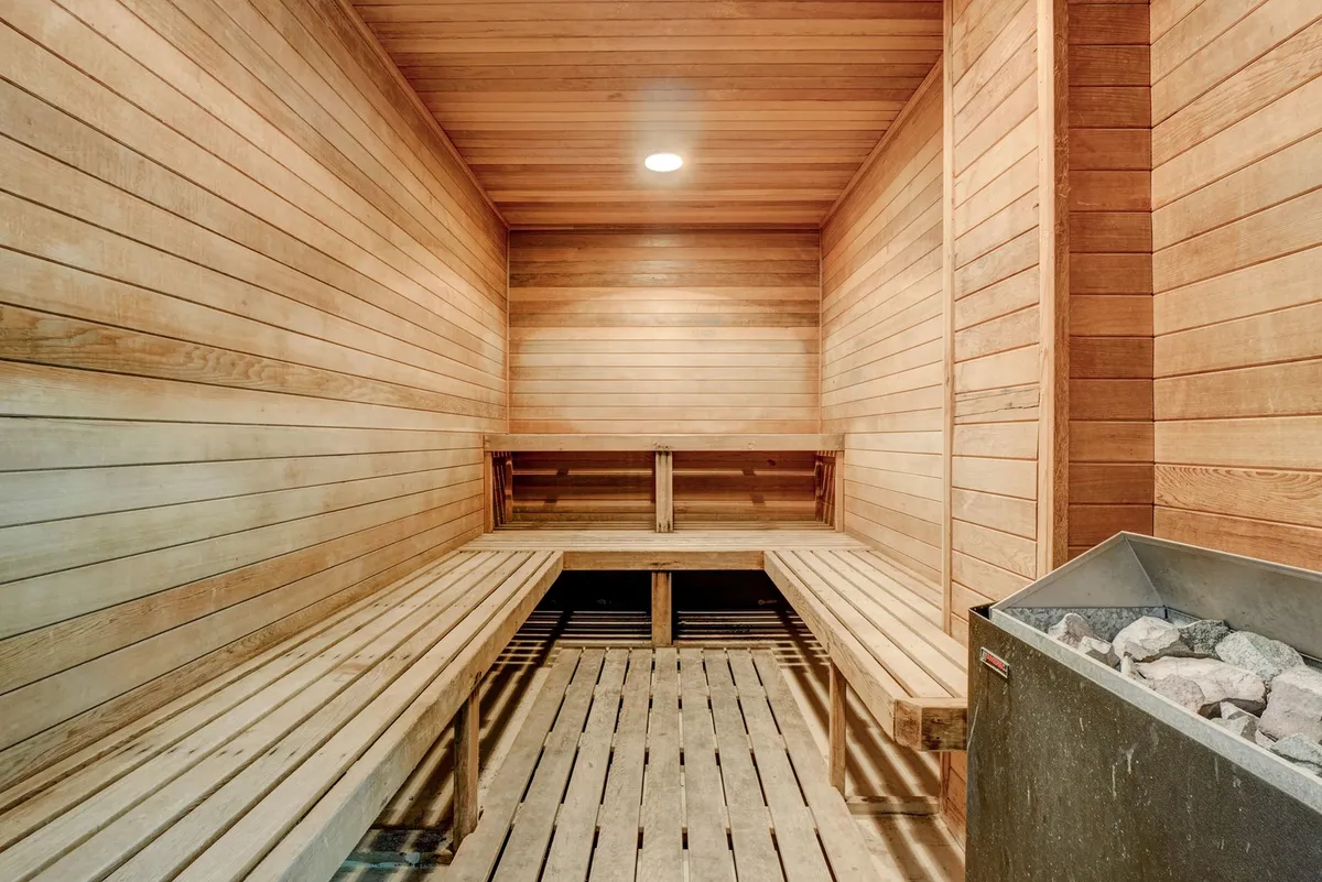 A tranquil sauna room with wooden benches and a stone sauna heater, creating a serene space for relaxation and post-workout recovery. The ambiance is calm and wellness-focused.
