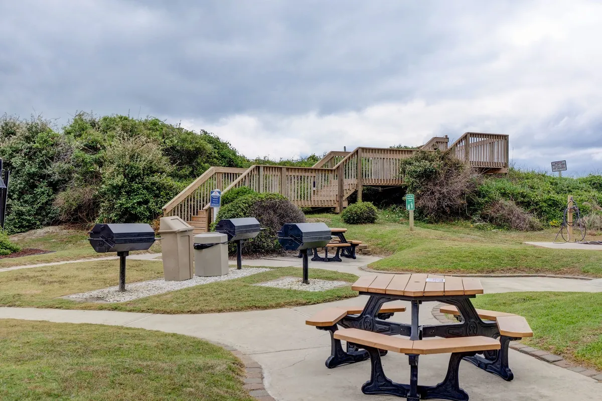 A relaxed outdoor setting with several picnic tables and grills, inviting groups to gather, socialize, and cook together in a communal space.
