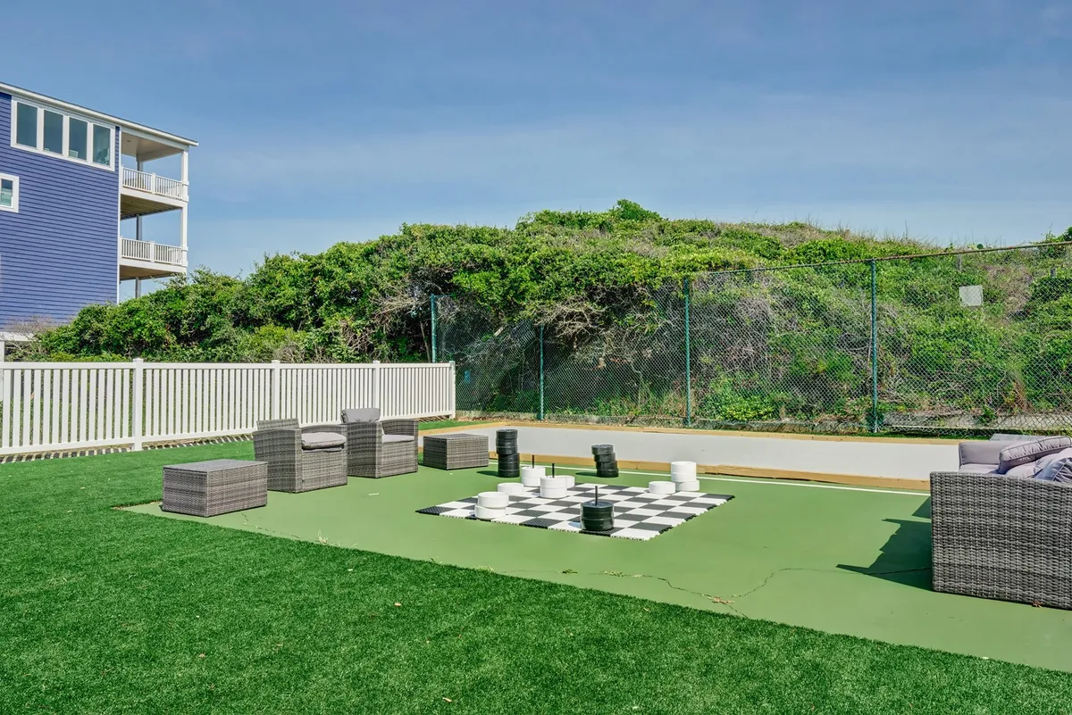 An inviting outdoor area featuring a large chess set with modern seating arrangements, surrounded by lush greenery. The space is designed for relaxation, social gatherings, and casual games under the sun.