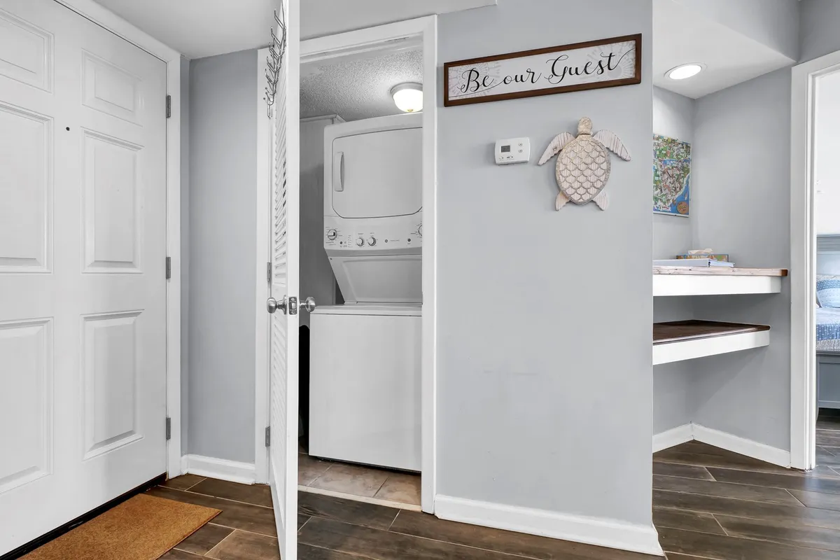 A cozy laundry area located near the front door, featuring a washer, dryer, shelf with books, and friendly turtle décor, contributing to the feel of home and convenience.