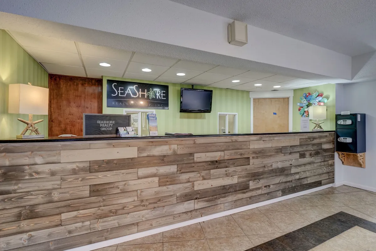 A welcoming reception area featuring a reception desk, SEASHORE sign, lighthouse-themed lamp, and TV screen, designed to provide first impressions of the property's beach-oriented hospitality and reliable local management.